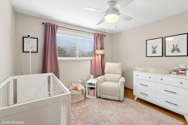 bedroom featuring a crib, wood finished floors, and ceiling fan