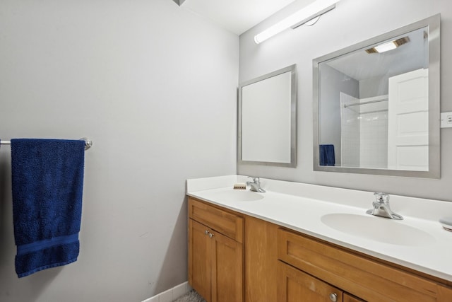 bathroom featuring double vanity, a shower, baseboards, and a sink
