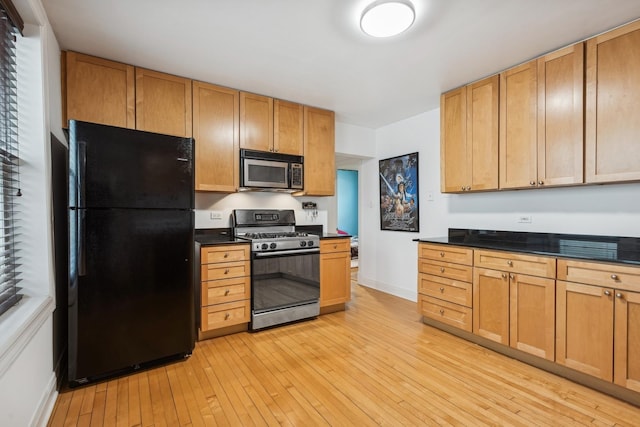 kitchen featuring stainless steel microwave, freestanding refrigerator, light wood-type flooring, gas range, and dark countertops