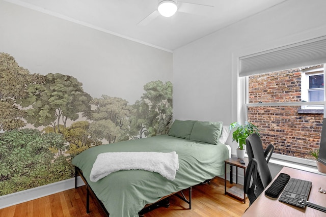 bedroom with wood finished floors, a ceiling fan, crown molding, brick wall, and baseboards