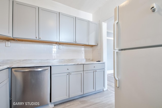kitchen with freestanding refrigerator, dishwasher, gray cabinetry, tasteful backsplash, and light wood-style flooring