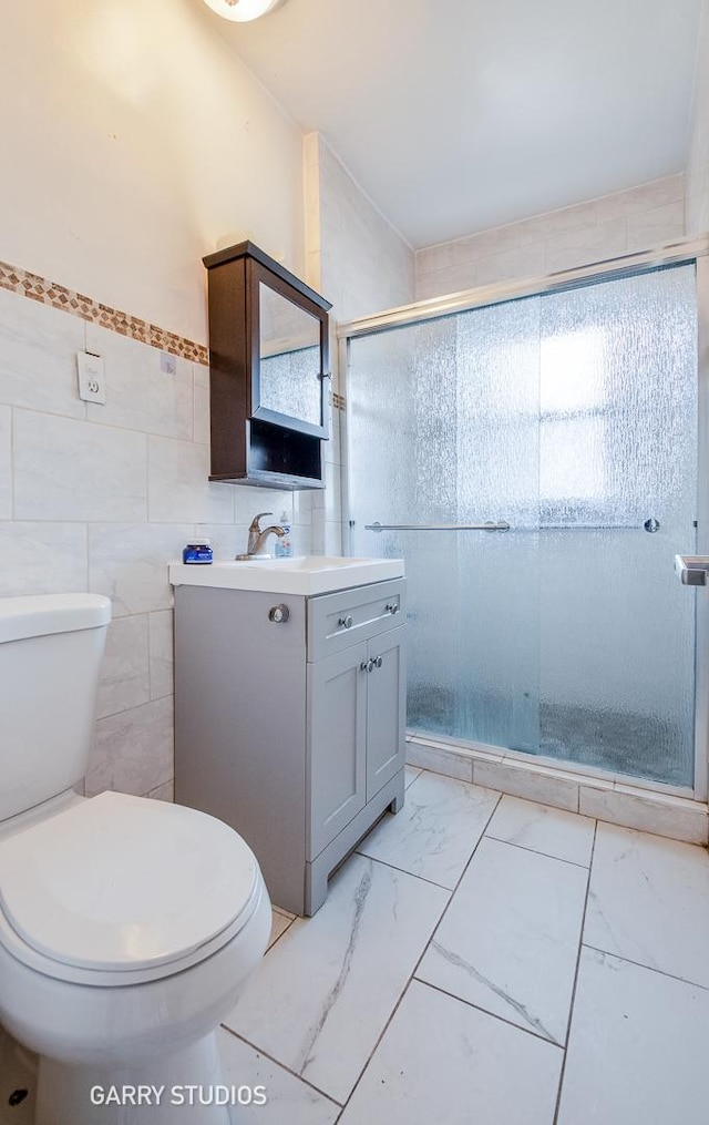 bathroom featuring tile walls, toilet, vanity, a shower stall, and marble look tile flooring