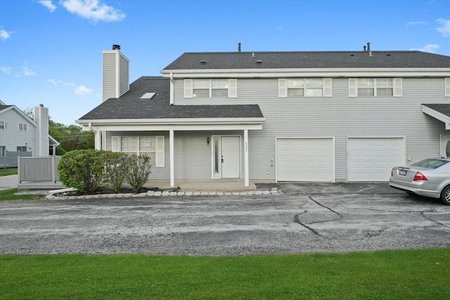 view of front of home with driveway, a garage, a chimney, and covered porch