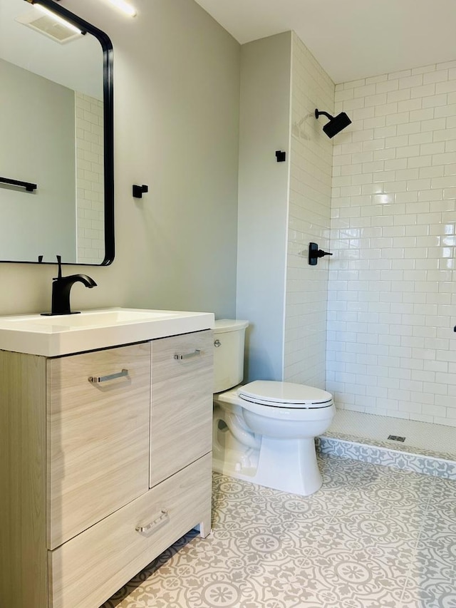 full bath with toilet, visible vents, a tile shower, tile patterned floors, and vanity