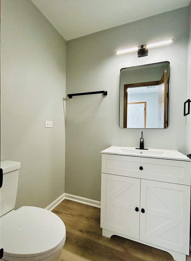 half bath with baseboards, vanity, toilet, and wood finished floors
