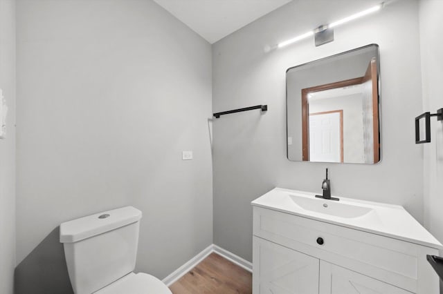 half bath with wood finished floors, toilet, vanity, and baseboards