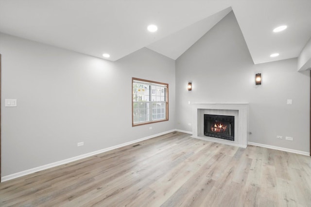 unfurnished living room with a fireplace with flush hearth, light wood finished floors, baseboards, vaulted ceiling, and recessed lighting