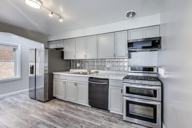 kitchen featuring stainless steel appliances, gray cabinetry, a sink, decorative backsplash, and light countertops