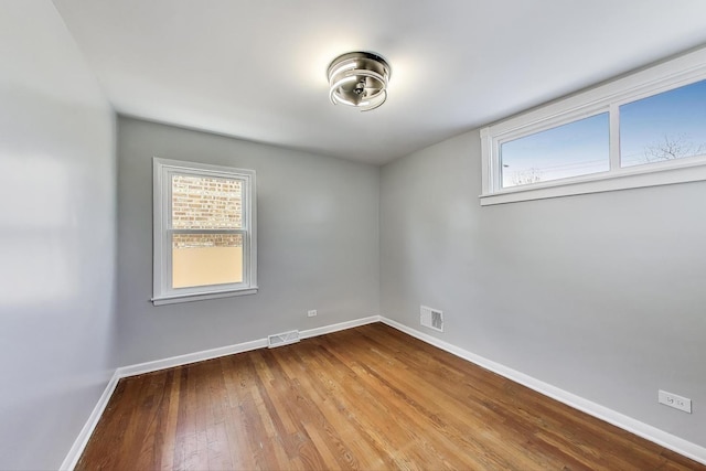empty room featuring wood finished floors, visible vents, and baseboards