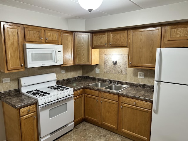 kitchen featuring brown cabinets, a sink, dark countertops, white appliances, and decorative backsplash
