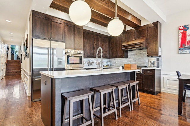 3940 N Ashland Ave Unit 2N, Chicago, IL 60613 - kitchen featuring stainless steel appliances, exhaust hood, light countertops, dark wood-style floors, and dark brown cabinetry