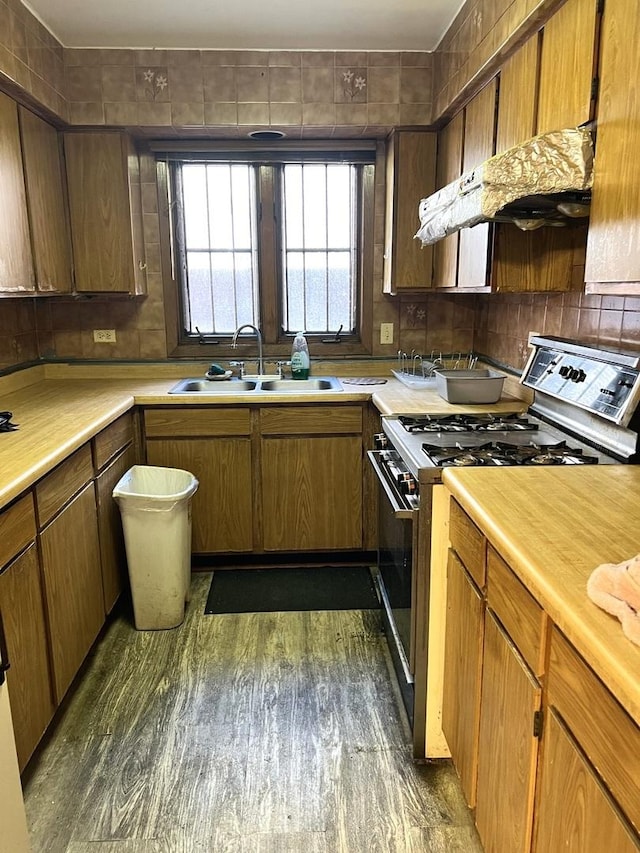 kitchen with stainless steel range with gas stovetop, a sink, dark wood-style floors, light countertops, and under cabinet range hood