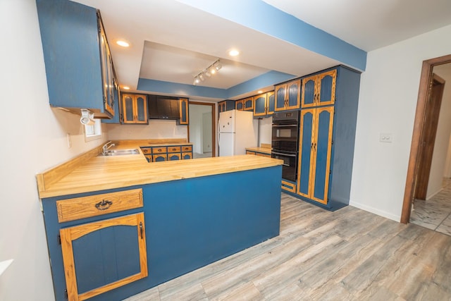 kitchen featuring freestanding refrigerator, a peninsula, a sink, glass insert cabinets, and light wood-style floors