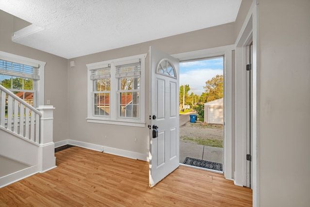 entrance foyer featuring a textured ceiling, light wood-style flooring, baseboards, and stairs