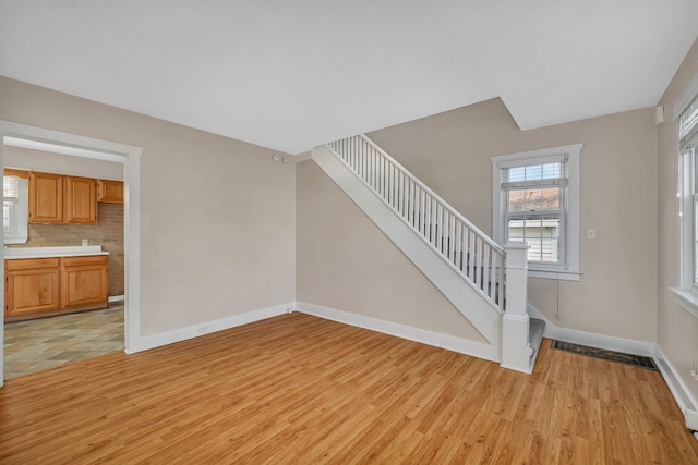 unfurnished living room with baseboards, stairway, and light wood finished floors