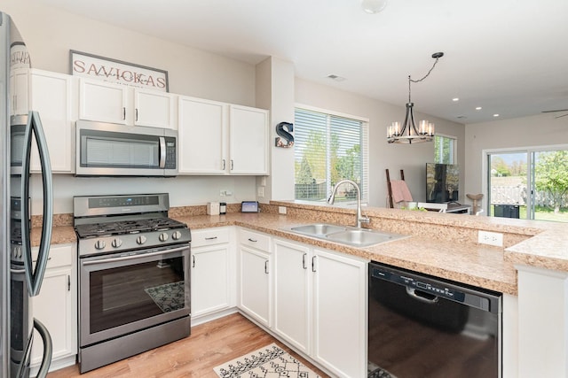 kitchen featuring stainless steel appliances, a sink, a peninsula, white cabinetry, and light wood-style floors
