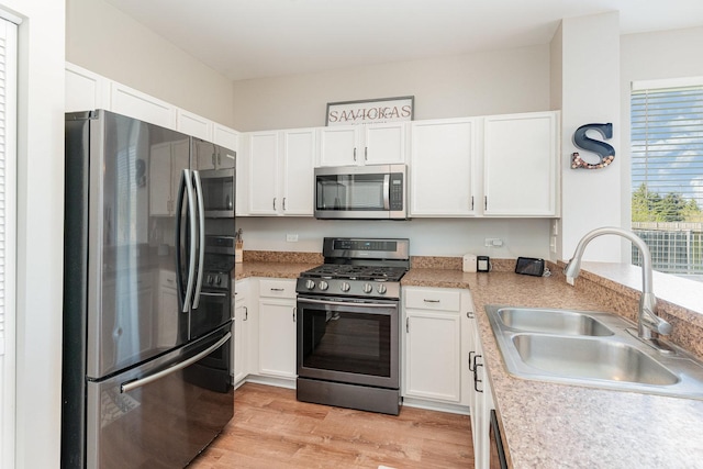 kitchen featuring stainless steel appliances, a sink, white cabinets, light wood-style floors, and light countertops