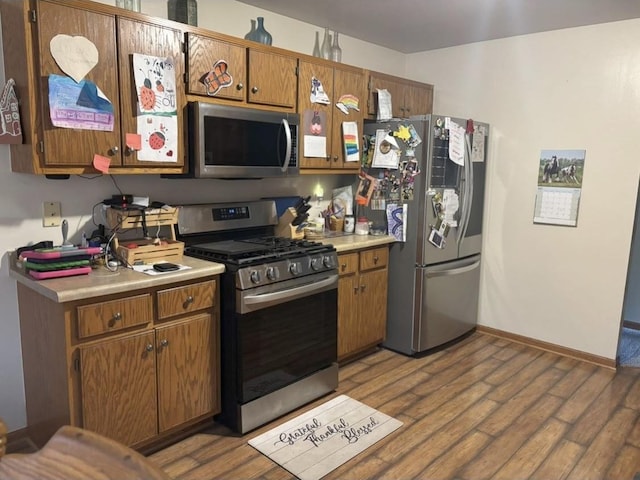 kitchen with brown cabinetry, light countertops, appliances with stainless steel finishes, and wood finished floors