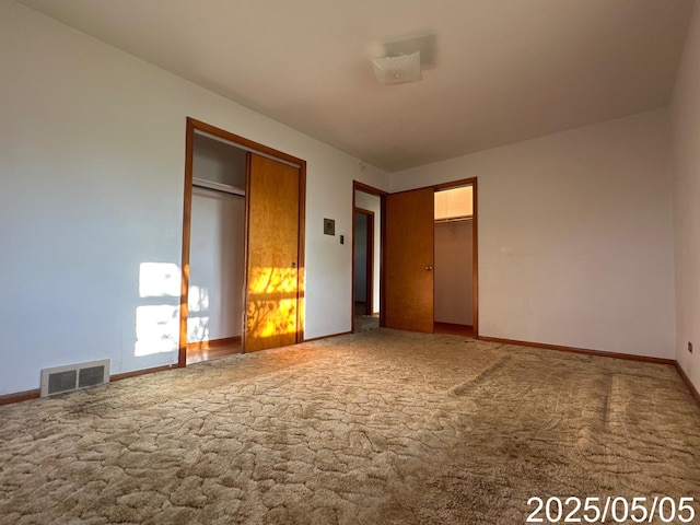 unfurnished bedroom featuring baseboards, two closets, visible vents, and carpet