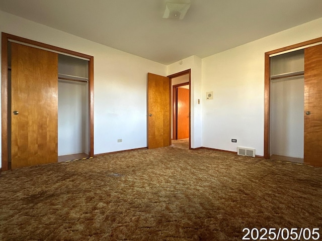 unfurnished bedroom featuring carpet, two closets, visible vents, and baseboards