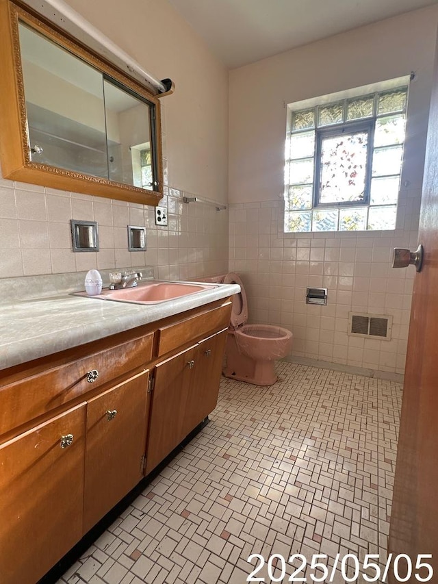 bathroom featuring toilet, tile walls, visible vents, brick patterned floor, and vanity