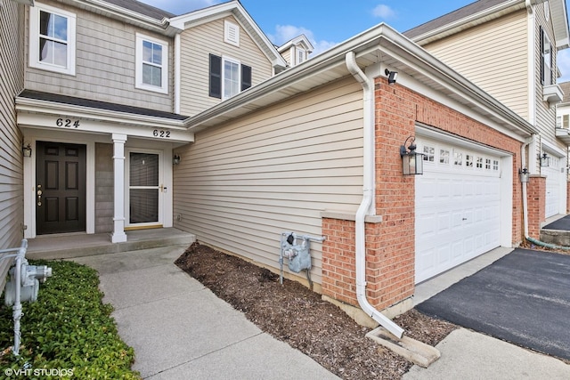 doorway to property with brick siding, asphalt driveway, and an attached garage