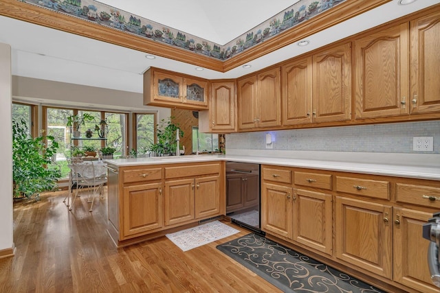 kitchen featuring a sink, light wood-style flooring, dishwashing machine, light countertops, and decorative backsplash