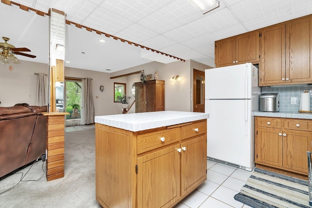 kitchen with freestanding refrigerator, tile counters, ceiling fan, and backsplash