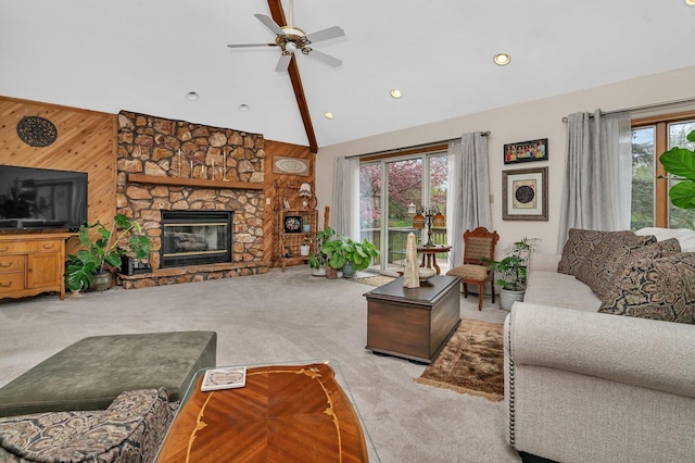 living room featuring carpet flooring, high vaulted ceiling, ceiling fan, a stone fireplace, and wood walls