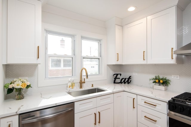 kitchen featuring a sink, wall chimney exhaust hood, white cabinets, backsplash, and appliances with stainless steel finishes