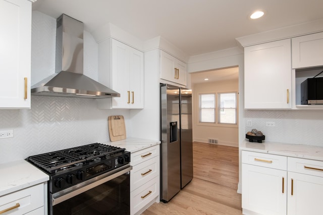 kitchen with light wood-style flooring, stainless steel fridge with ice dispenser, wall chimney exhaust hood, black range with gas stovetop, and white cabinets