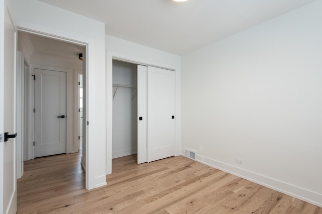 unfurnished bedroom featuring baseboards, light wood-style floors, a closet, and visible vents