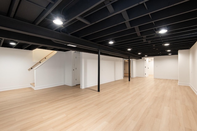 finished basement featuring stairway, baseboards, and light wood-type flooring