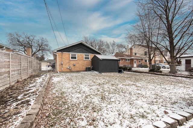 snow covered rear of property with brick siding, an outdoor structure, a shed, central air condition unit, and a fenced backyard