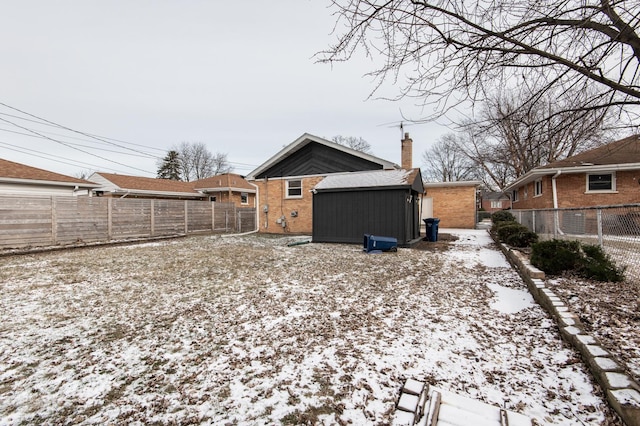 snow covered property featuring brick siding, an outdoor structure, a chimney, and a fenced backyard