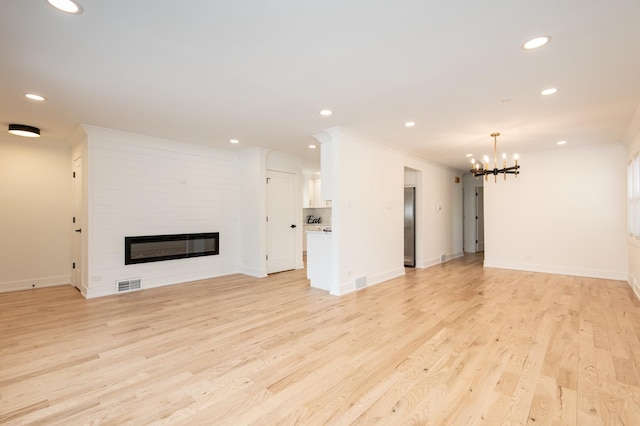 unfurnished living room featuring light wood finished floors, an inviting chandelier, visible vents, a large fireplace, and recessed lighting