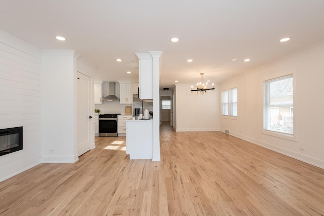 kitchen with stainless steel appliances, open floor plan, a chandelier, wall chimney exhaust hood, and light countertops
