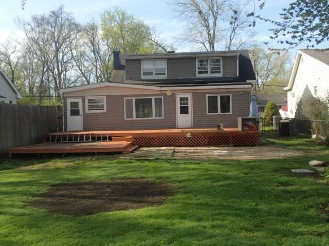 back of property featuring fence, a wooden deck, and a lawn