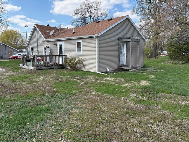 rear view of house featuring a deck, a shingled roof, and a yard