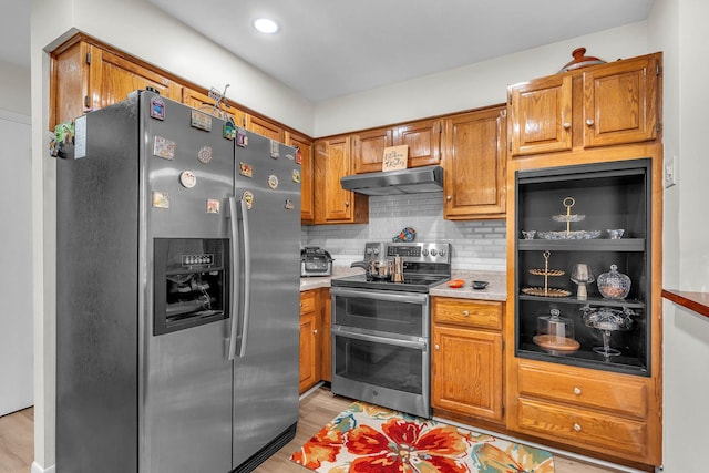 kitchen with brown cabinets, extractor fan, light wood-type flooring, appliances with stainless steel finishes, and decorative backsplash