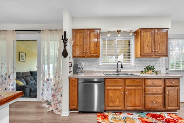 kitchen featuring light wood finished floors, brown cabinets, a sink, dishwasher, and tasteful backsplash