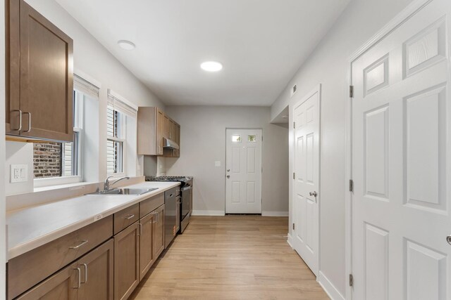 kitchen featuring a sink, light wood finished floors, appliances with stainless steel finishes, light countertops, and baseboards