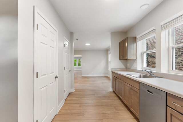 kitchen featuring stainless steel dishwasher, light wood-type flooring, baseboards, a sink, and light countertops