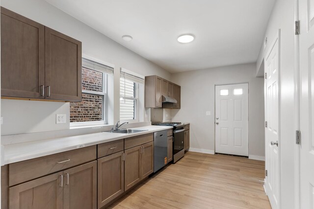 kitchen with a sink, appliances with stainless steel finishes, light wood-style flooring, light countertops, and under cabinet range hood
