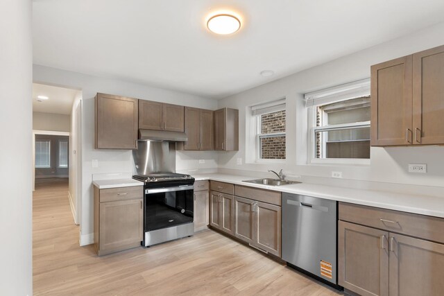 kitchen featuring stainless steel appliances, a sink, light wood finished floors, under cabinet range hood, and light countertops