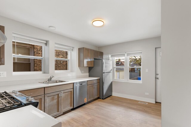 kitchen with stainless steel appliances, a sink, light wood-style flooring, light countertops, and baseboards