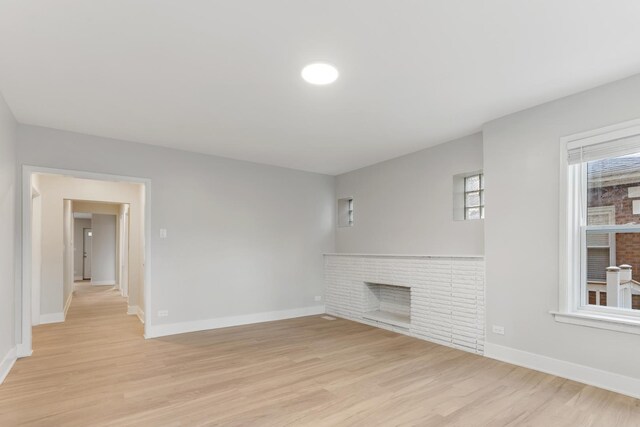 unfurnished living room with a fireplace, light wood-type flooring, and baseboards