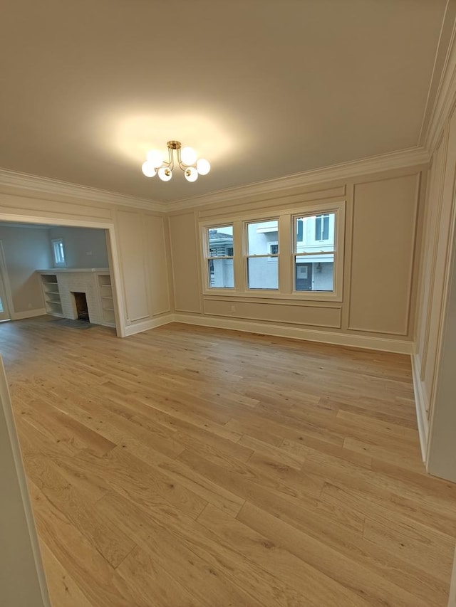 unfurnished living room with light wood-style flooring, ornamental molding, a decorative wall, a chandelier, and a fireplace with flush hearth
