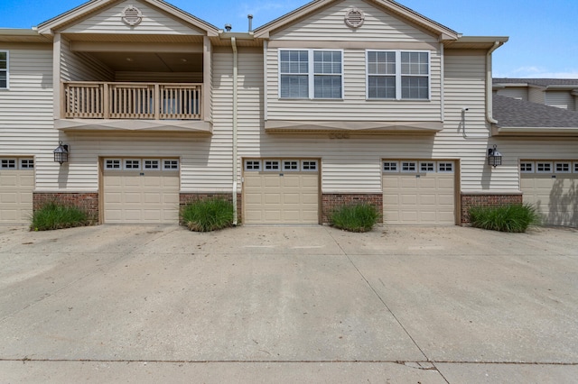 view of property featuring brick siding, a garage, a balcony, and driveway