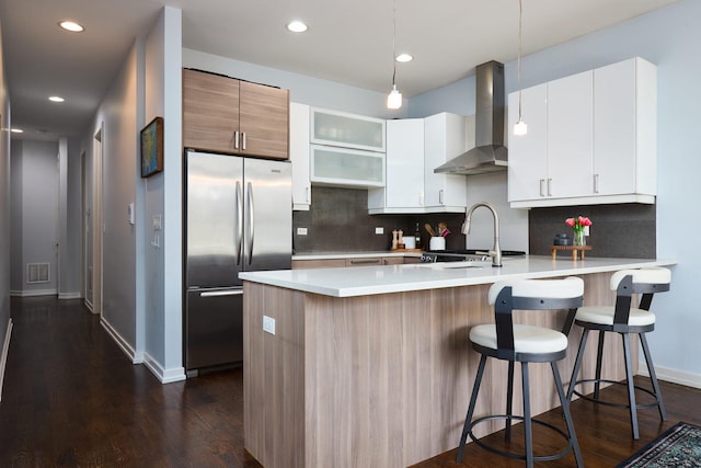 kitchen featuring stainless steel refrigerator, wall chimney exhaust hood, a peninsula, backsplash, and recessed lighting
